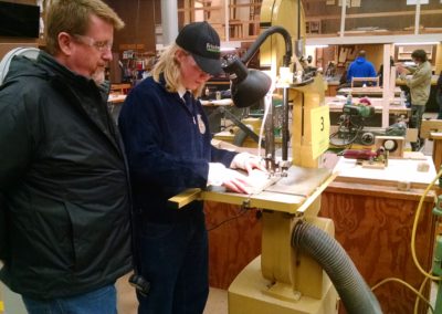Instructor watches students using a jigsaw to cut wood
