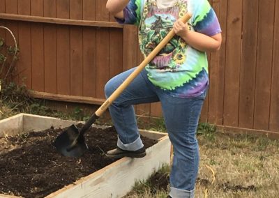 Student poses with shovel while smoothing out soil in a planter box