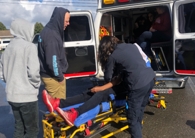 Students practice using a gurney to transport a patient into an open ambulance