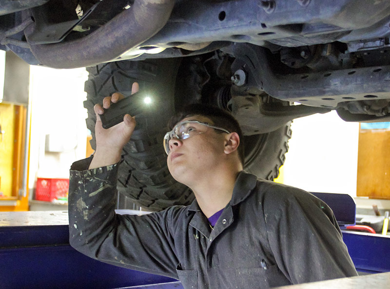 A student examining the underside of a vehicle