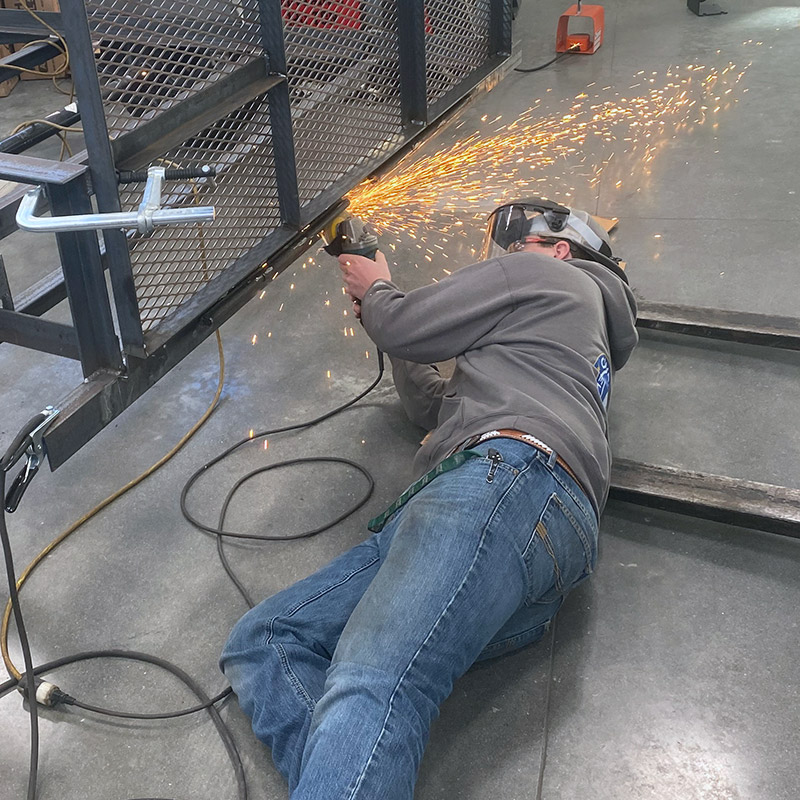 A student using a grinder on a metal trailer